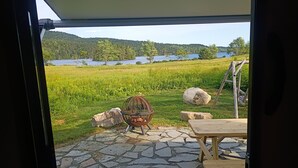 Terassi, jossa on kivilaattalattia, metallituoli, puupöytä sekä näkymä järvelle ja metsään.