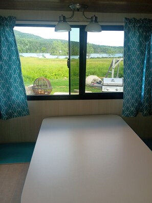A room with a bed, a window with curtains, a view of a green landscape, and a barbecue grill outside. - Ponds view
Acadia National Park (Tremont)