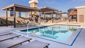 A rooftop pool with lounge chairs, a covered seating area, and a view of the city skyline.