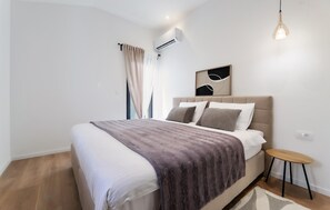 A modern bedroom with a bed, a bedside table, a hanging light, and an air conditioning unit. - Pet friendly home in Krk (Krk)