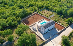 Ein weißes Gebäude mit Schwimmbad und Solaranlage, umgeben von üppiger Vegetation.