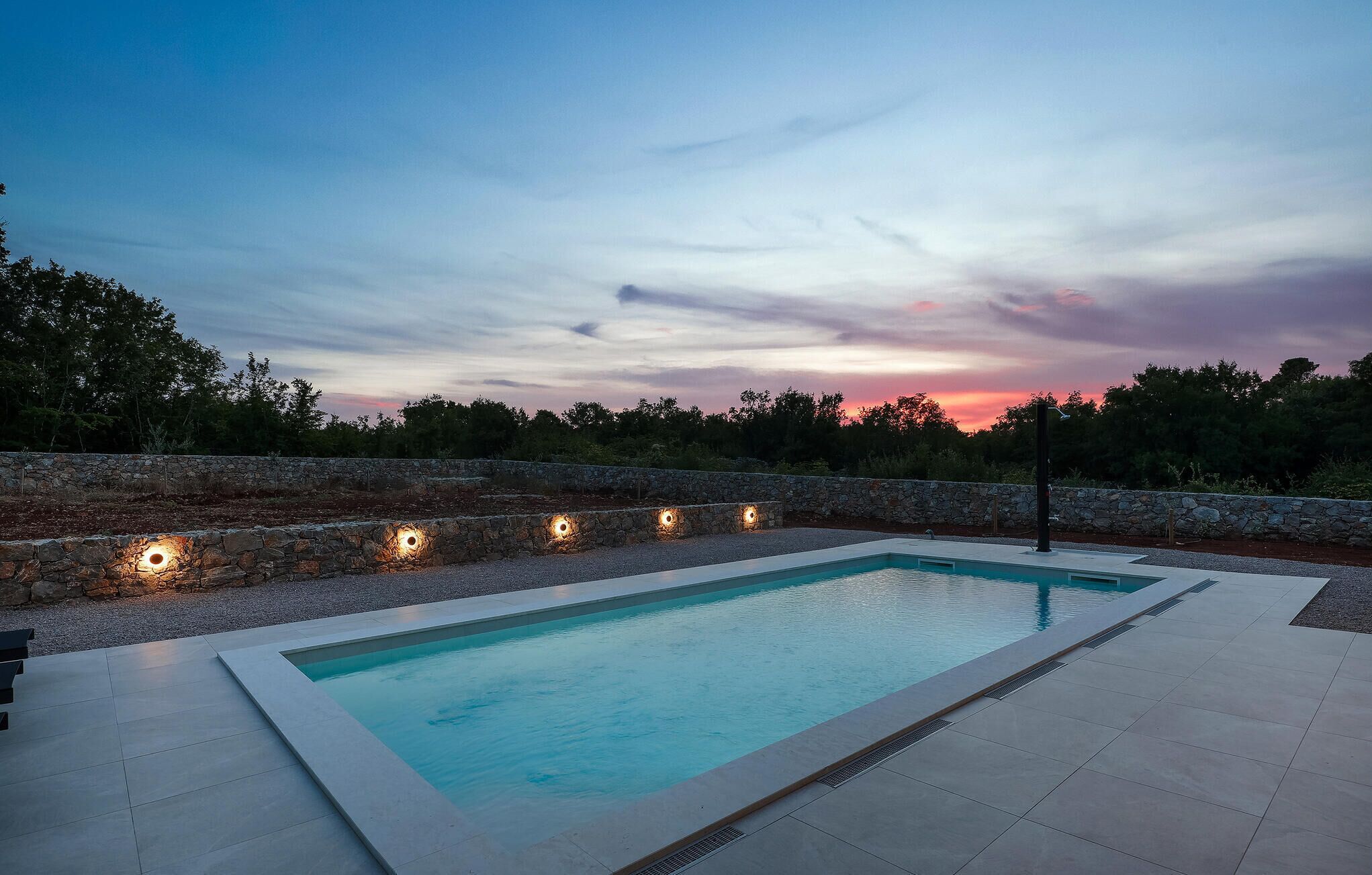 Ein rechteckiger Pool mit Steinmauer und Beleuchtung am Rand.