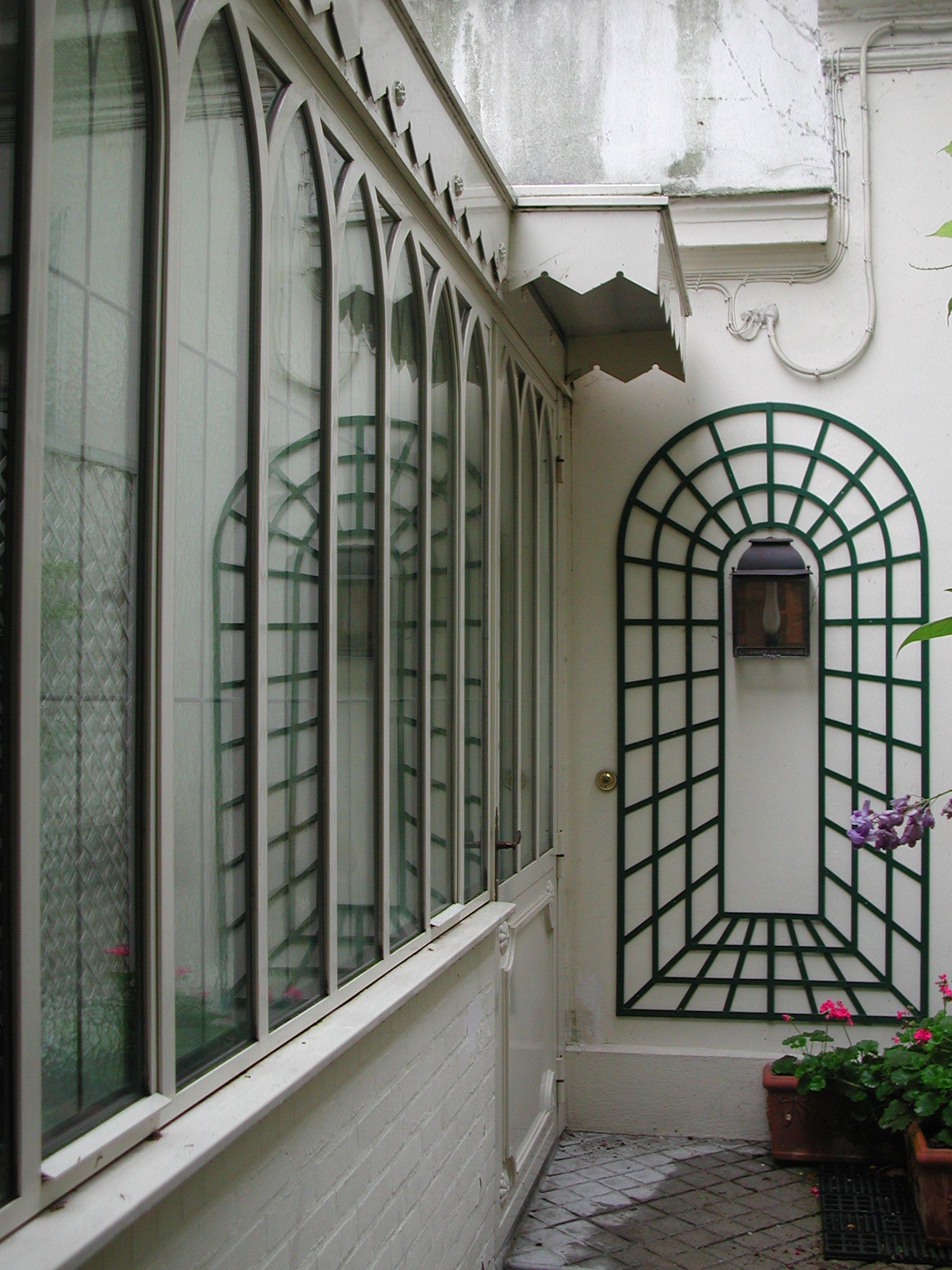 A narrow corridor with a white brick wall, a green metal gate, and a window with a grid pattern.