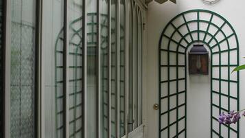 A narrow corridor with a white brick wall, a green metal gate, and a window with a grid pattern.