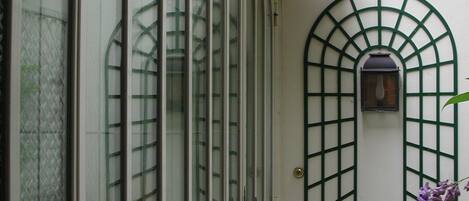 A narrow corridor with a white brick wall, a green metal gate, and a window with a grid pattern.