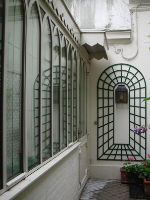 A narrow corridor with a white brick wall, a green metal gate, and a window with a grid pattern. - Atypical, rare house in the historic and quiet heart of Paris (Paris)