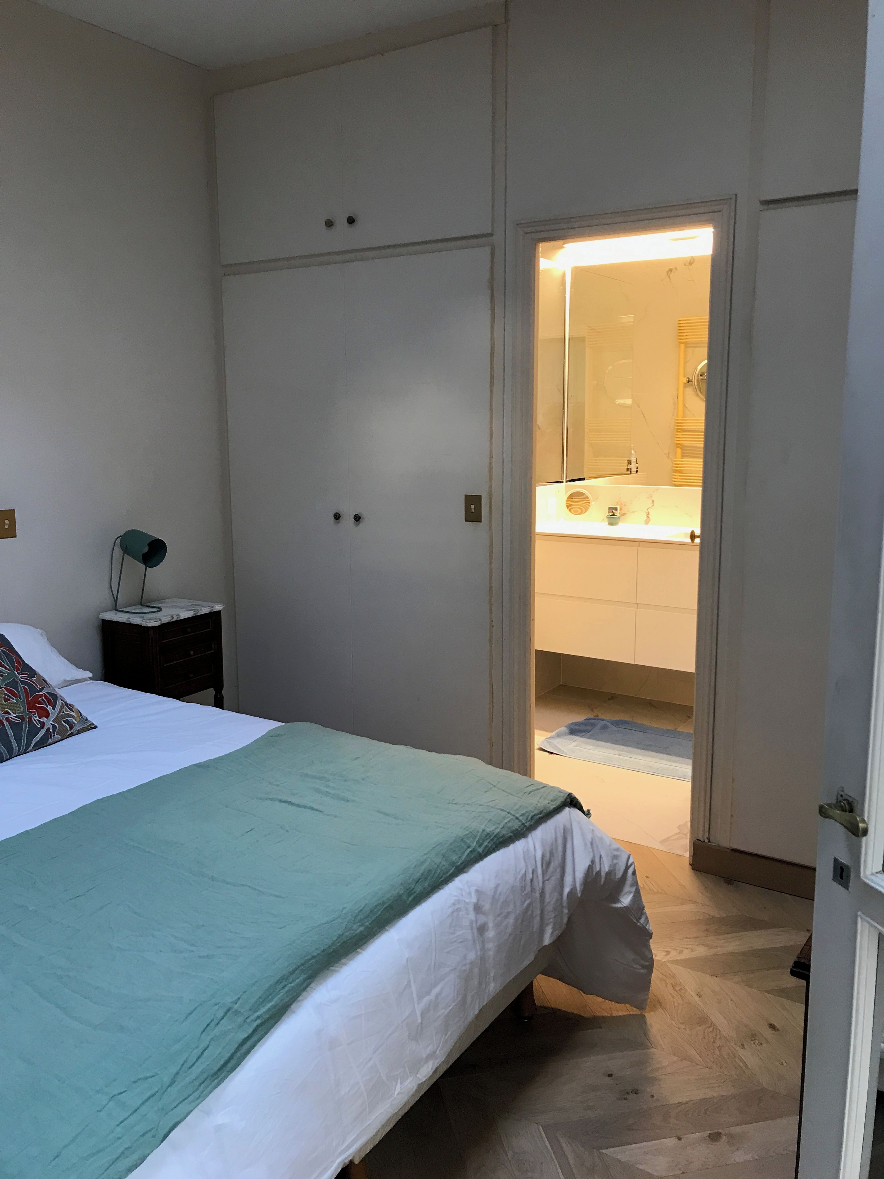 A bedroom with a bed, a nightstand, a wardrobe, and an open door leading to a bathroom.