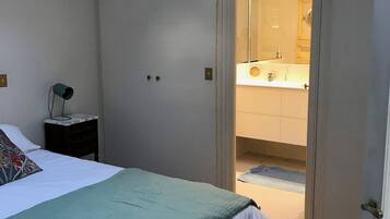 A bedroom with a bed, a nightstand, a wardrobe, and an open door leading to a bathroom.