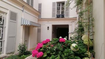 A courtyard with a building featuring a balcony, a door, and a window with shutters.