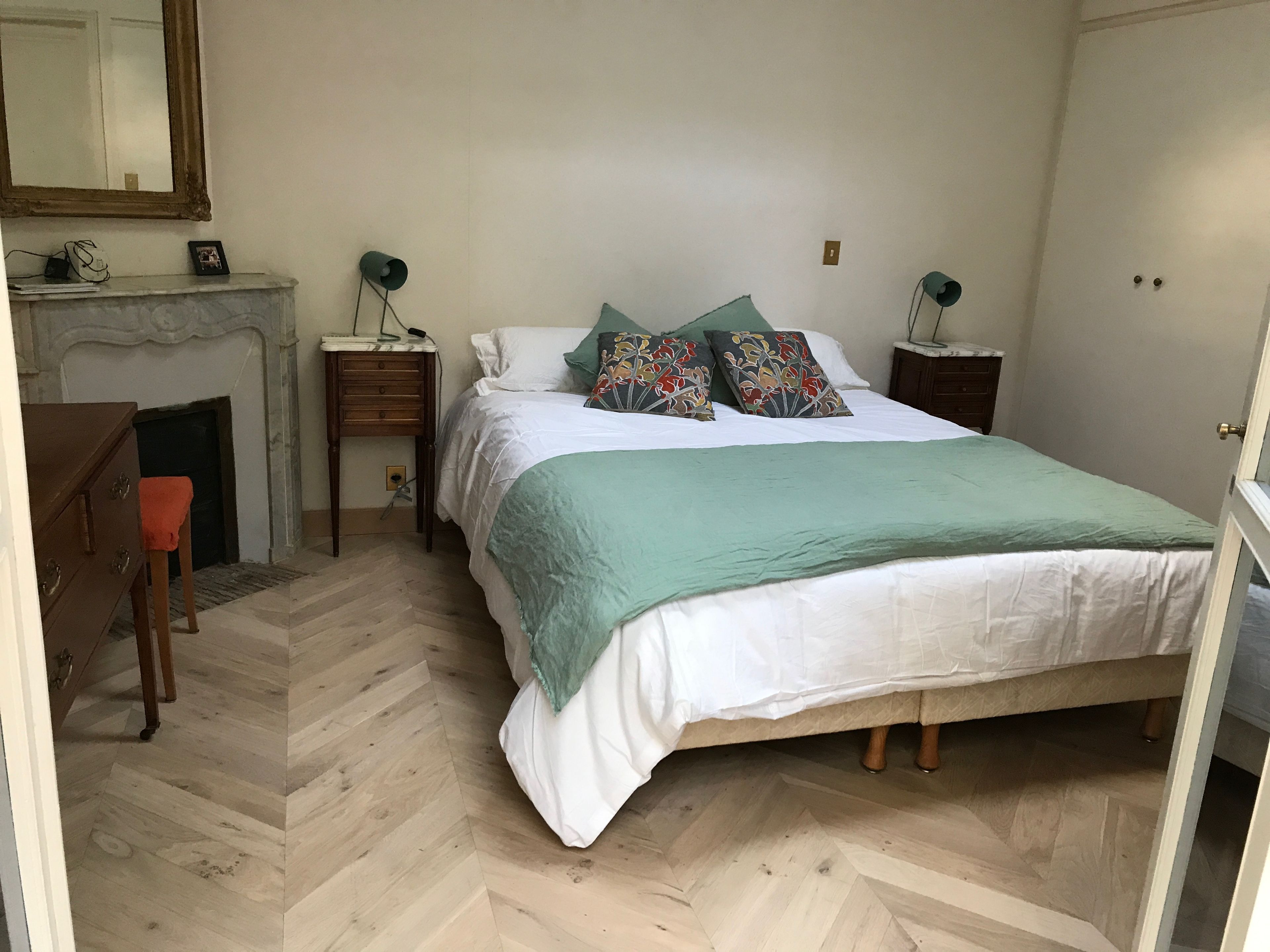 Une chambre à coucher comprenant un lit, une commode, une chaise, une table de chevet, une lampe, un miroir et une cheminée.