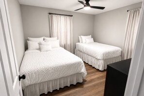 A bedroom with two beds, a ceiling fan, and a wooden floor. - Newly Renovated 3BR Home - Near Raleigh - Sleeps 7 (Zebulon)