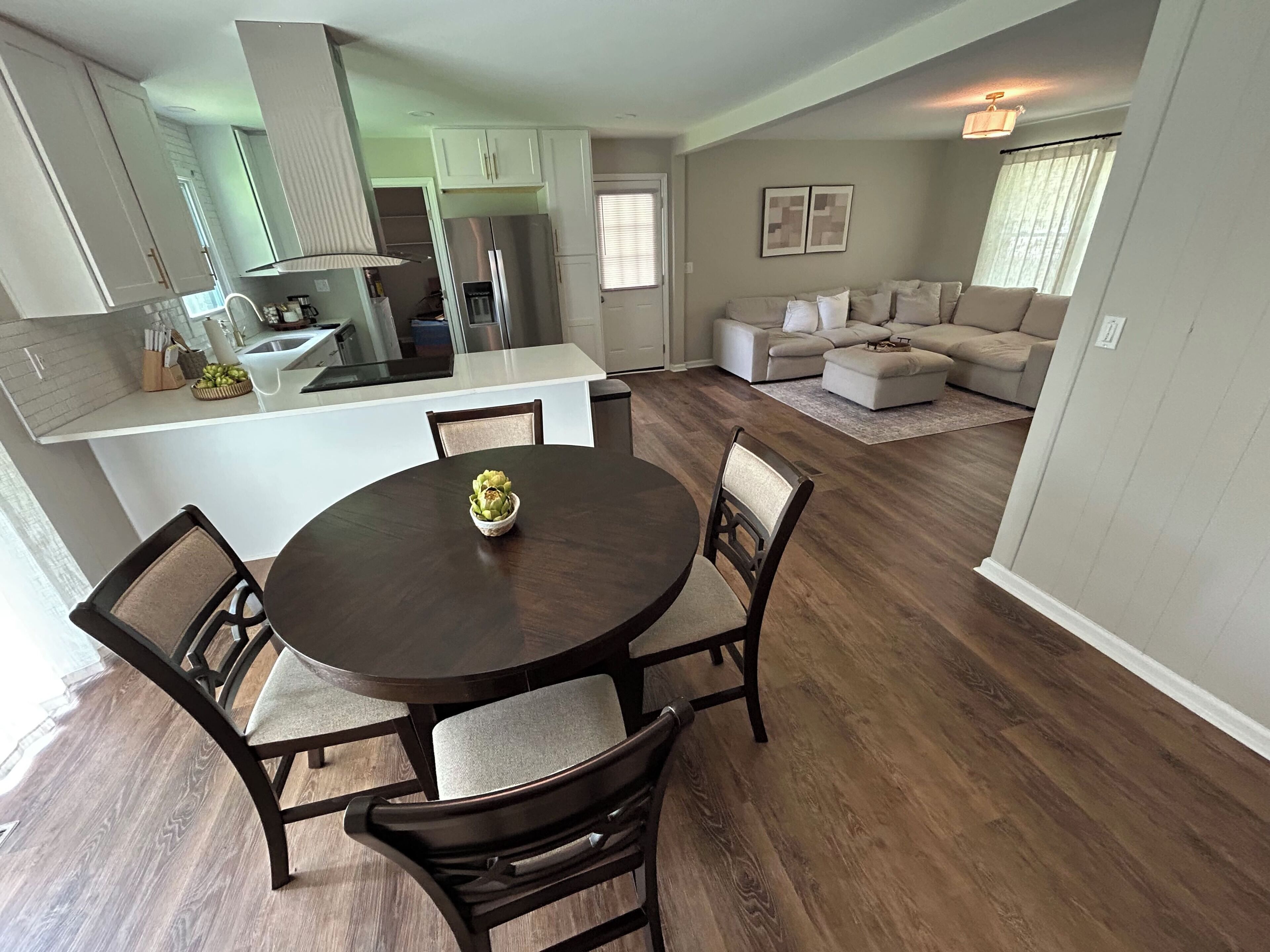 A modern kitchen with white cabinets, a central island, and a dining area with a round table and chairs.
