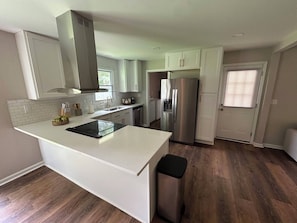 A modern kitchen with white cabinetry, a stainless steel refrigerator, and a central island. - Newly Renovated 3BR Home - Near Raleigh - Sleeps 7 (Zebulon)