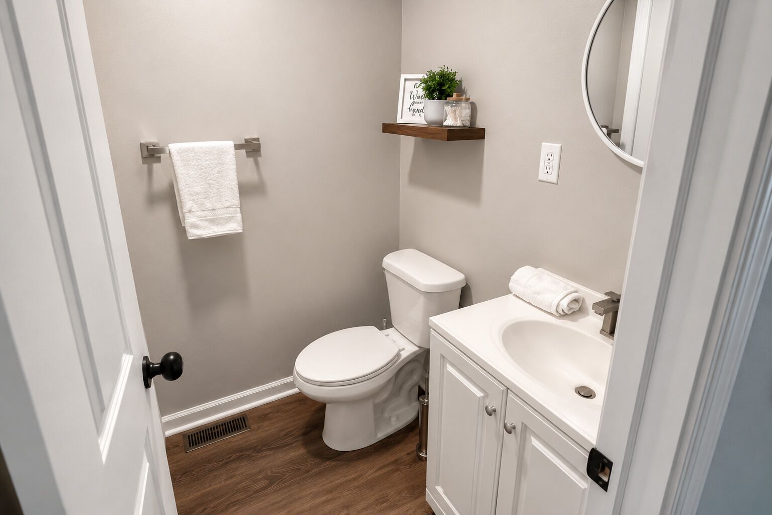 A small bathroom with a toilet, sink, and a shelf with a plant and a framed quote.