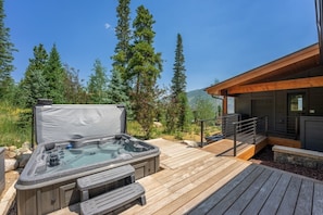 Jacuzzi en una terraza de madera con vista a las montañas, un edificio de madera con balcón y barandilla de metal.