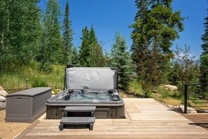 A hot tub with a bench, surrounded by a wooden deck and a metal railing, set in a forested area. - Ultra-Luxury Mountain Retreat w/ Sauna & Hot Tub | Summit Sky Ranch (Silverthorne)