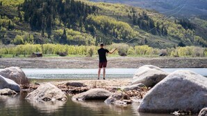 Una persona pescando en un río con montañas al fondo.