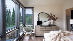 Un dormitorio con una ventana grande, una silla, un aparador, un espejo y una cama.