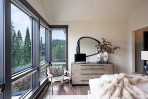 Ein Schlafzimmer mit großem Fenster, einem Sessel, einem Schminktisch und einem Bett.