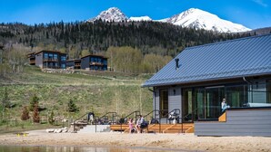Un moderno albergue con un amplio ventanal, una terraza de madera y vistas a la montaña.