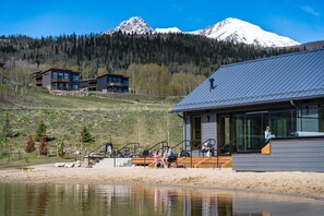 Ein modernes Lodge-Gebäude mit großer Glasfassade, einer Holzterrasse und Blick auf einen Berg.
