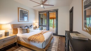 Un dormitorio con cama, mesitas de noche, ventilador de techo, ventana y puerta que da a un espacio exterior.