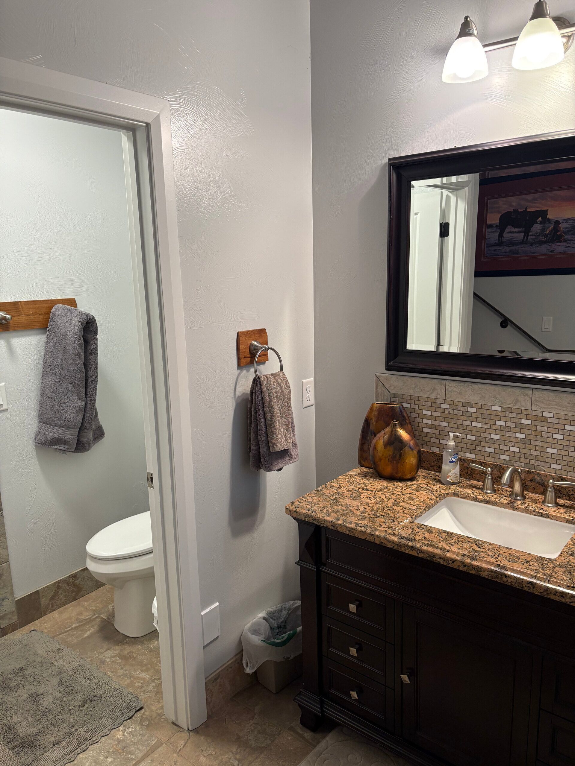 A bathroom with a toilet, sink, vanity, towel rack, and a mirror with a picture.