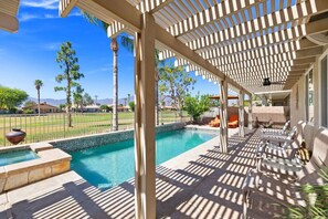 Ein Poolbereich mit Pergola, Liegestühlen und Blick auf einen Golfplatz.