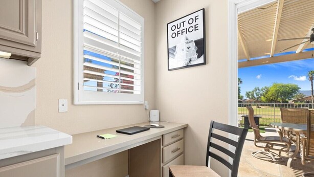 A room with a desk, chair, and a view of a balcony with outdoor furniture. - The Royal Fairway | 5BR/4BA Pool, Spa & Golf Views (Indio)