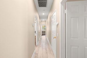 A hallway with beige walls, white doors, and a light wooden floor. - The Royal Fairway | 5BR/4BA Pool, Spa & Golf Views (Indio)