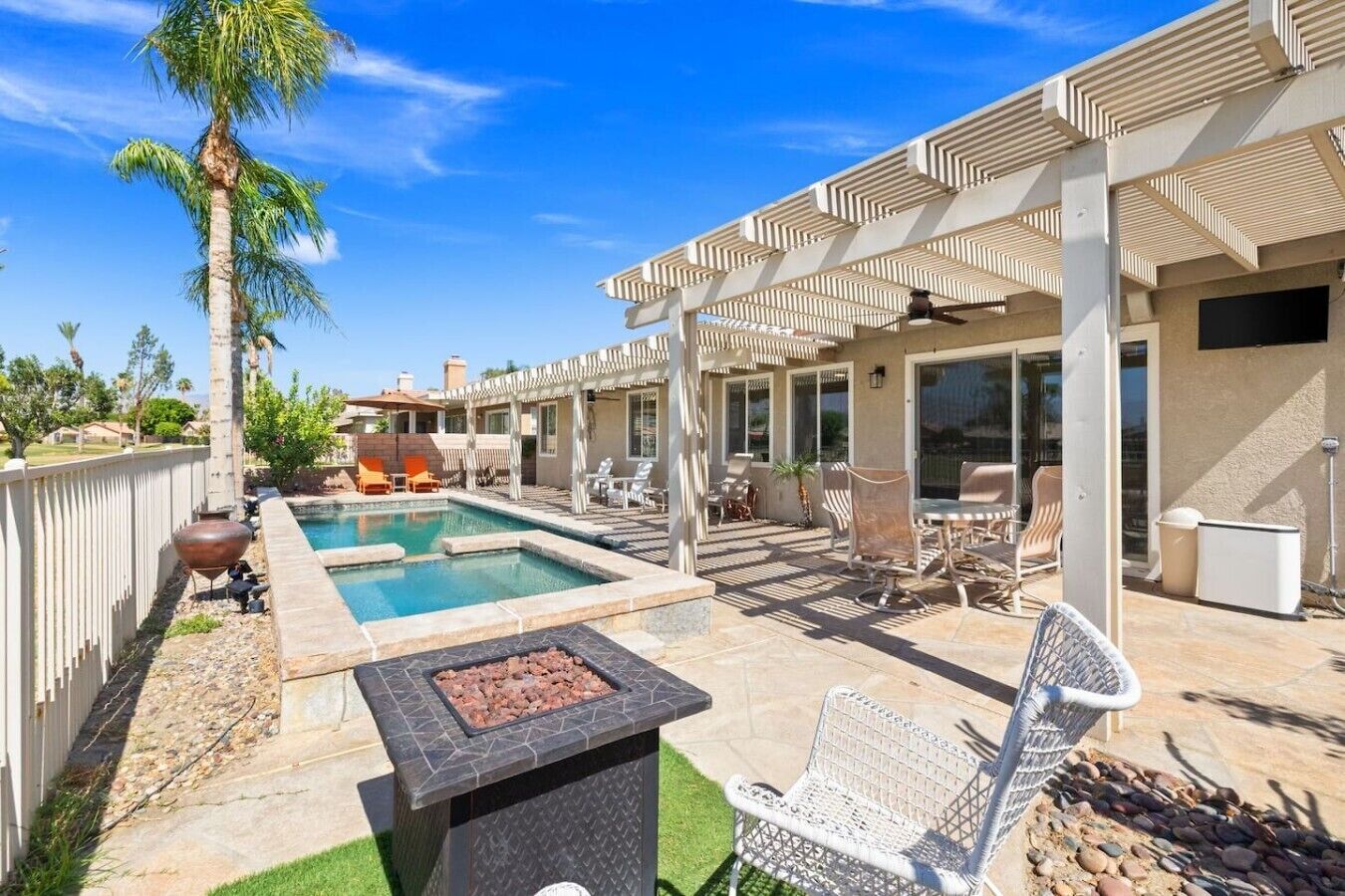 Un patio trasero con piscina, mobiliario exterior y un pérgola.