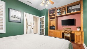 A bedroom with a bed, a desk, a chair, a television, and a bookshelf. - The Royal Fairway | 5BR/4BA Pool, Spa & Golf Views (Indio)