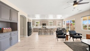 A spacious kitchen with a central island, grey cabinets, and a ceiling fan. - The Royal Fairway | 5BR/4BA Pool, Spa & Golf Views (Indio)