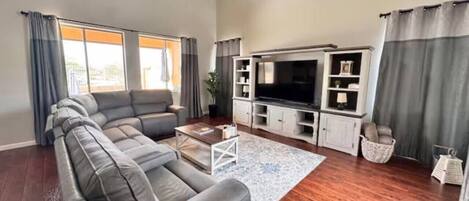 Ein geräumiges Wohnzimmer mit einer Eckcouch, einem Flachbildfernseher und Holzboden.