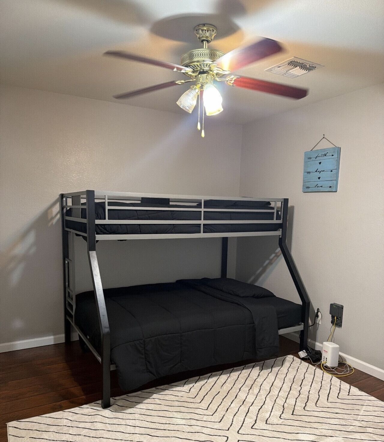 A bunk bed with a ceiling fan, a wall-mounted sign, and a power outlet.