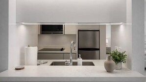 Cocina moderna con pileta de acero inoxidable, encimera de mármol e iluminación debajo de los armarios.