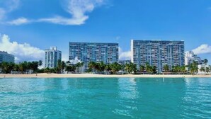 Un hotel frente a la playa con edificios altos, una playa de arena y agua azul cristalina.