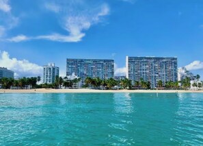 Ein Strandhotel mit hohen Gebäuden, einem Sandstrand und klarem, blauem Wasser.