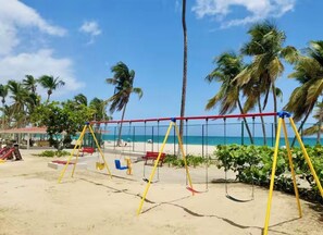 Une plage avec des balançoires, des palmiers et un ciel dégagé.