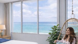 Un dormitorio con una cama, una silla colgante, una planta en maceta y vistas al océano.