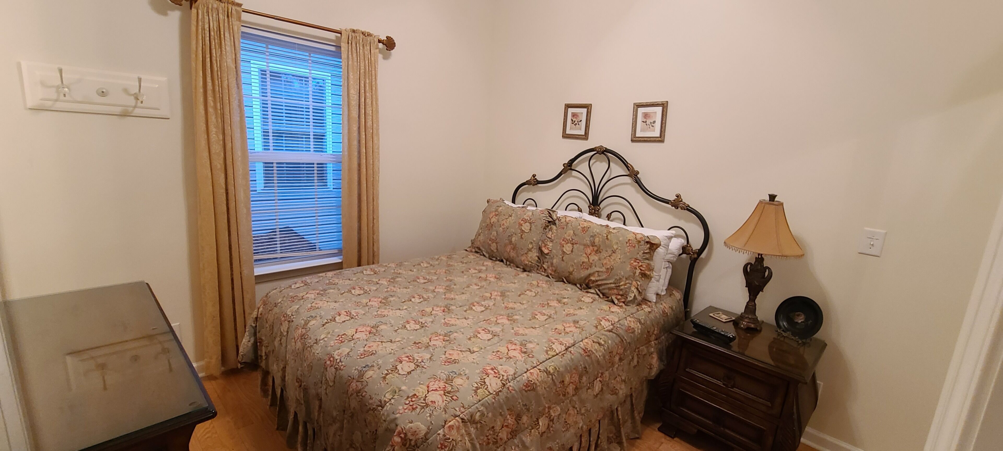 Un dormitorio con una cama, una mesita de noche, una lámpara y una ventana con cortinas.