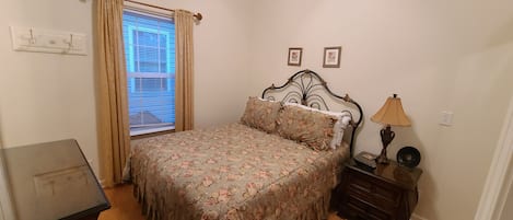 Un dormitorio con una cama, una mesita de noche, una lámpara y una ventana con cortinas.