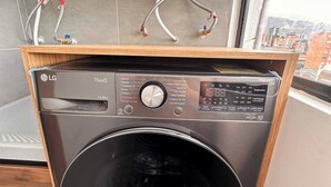 En kompakt, frontmatad tvättmaskin från LG ThinQ med en digital kontrollpanel, placerad i ett träskåp.