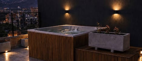 Terraza en la azotea con jacuzzi, zona de estar y dos copas de vino tinto sobre una mesa.