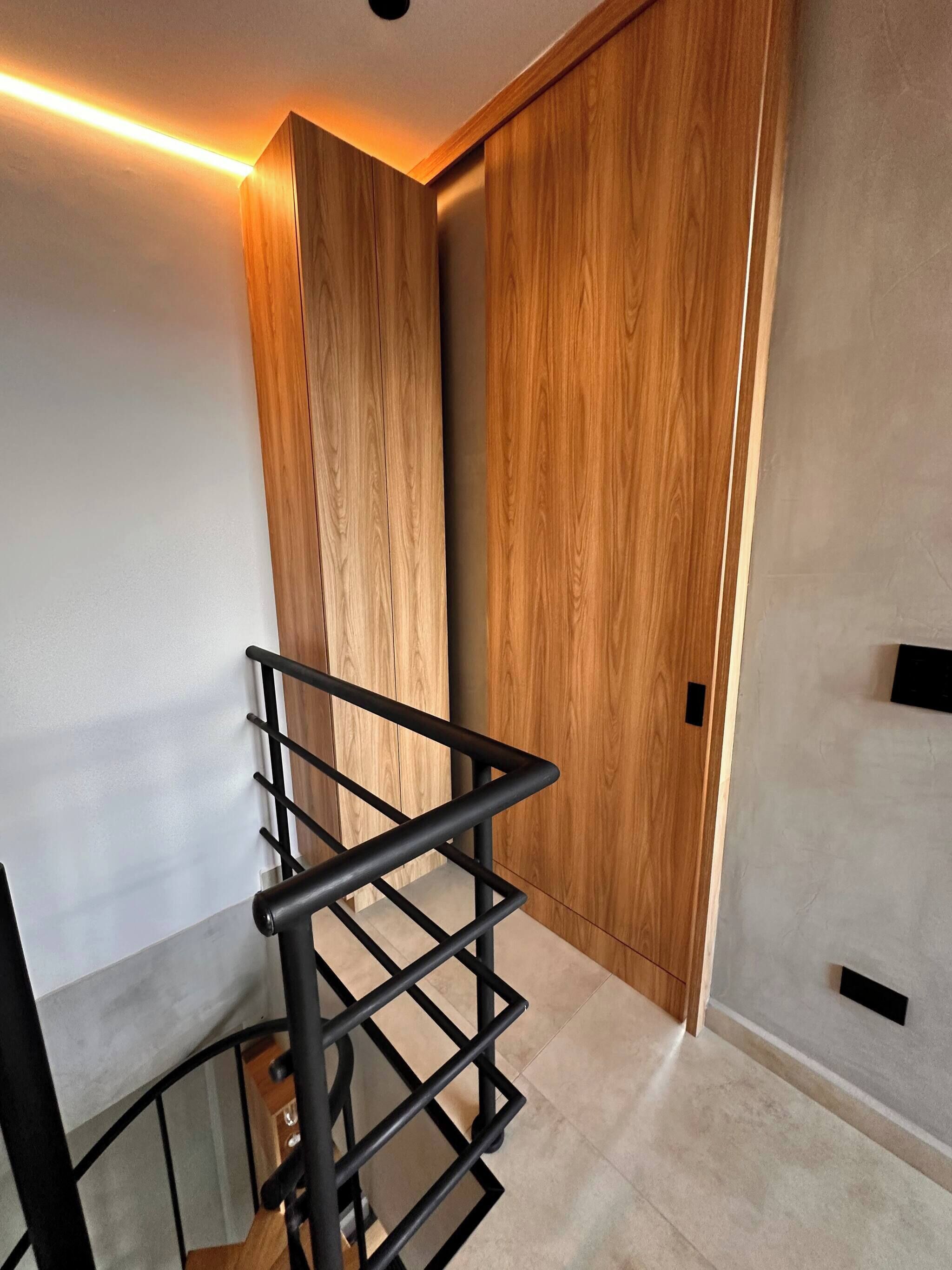 Un intérieur moderne avec une armoire en bois, une étagère en métal noir et un sol carrelé.