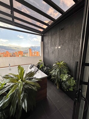 A modern bathroom with a skylight, a bathtub, and large potted plants. - Luxury PH Whirlpool Tub AC Fast Wifi (Medellín)