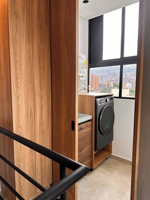 A laundry room with a washing machine, a window with a view of a cityscape, and wooden paneling. - Luxury PH Whirlpool Tub AC Fast Wifi (Medellín)