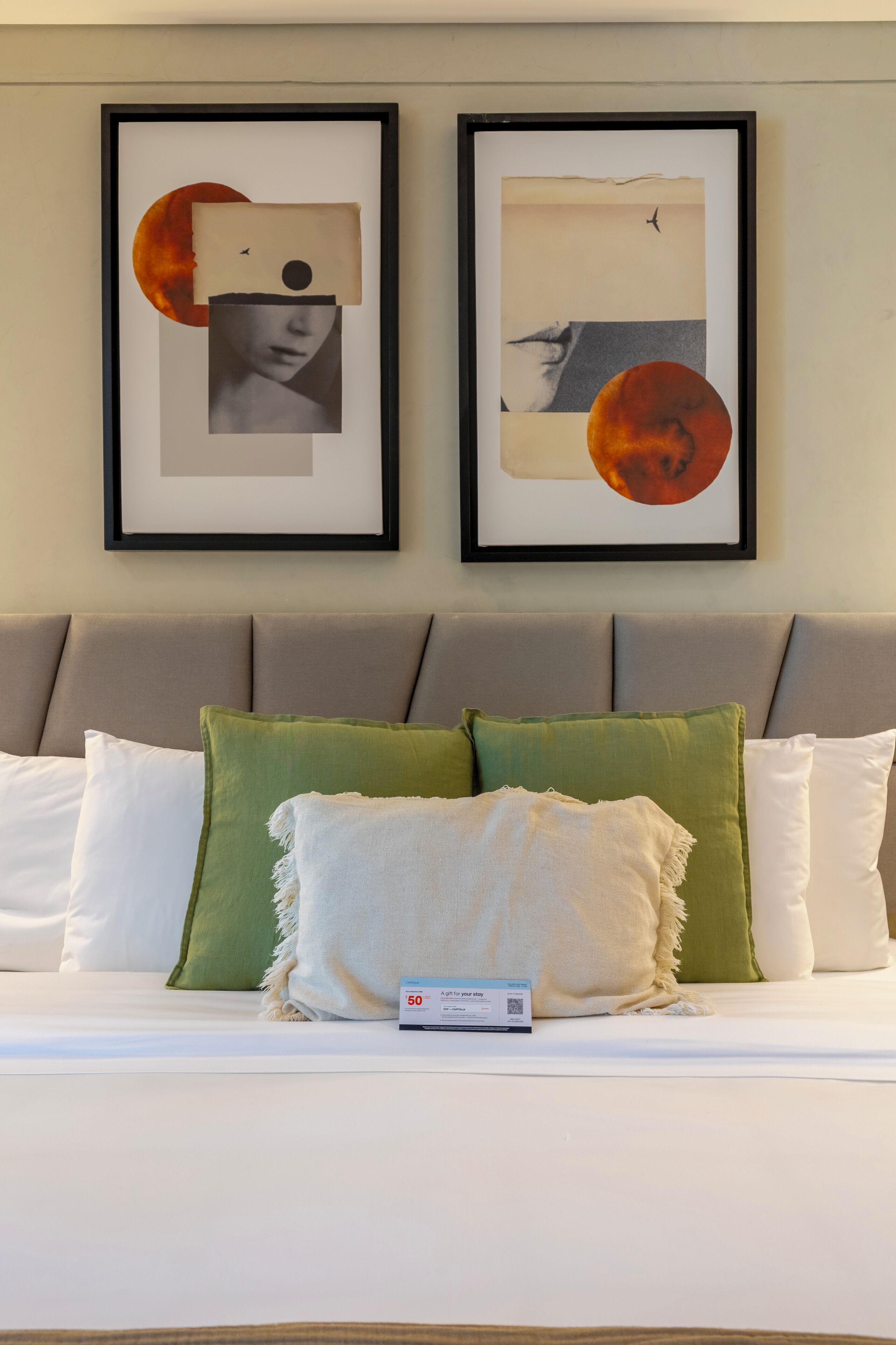 Een bed met een wit en groen kussenarrangement, een lijst met abstracte kunst erboven en een kaart op het bed.