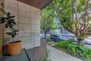 Un edificio moderno con fachada de tejas, una planta en maceta y vistas a coches aparcados y árboles.