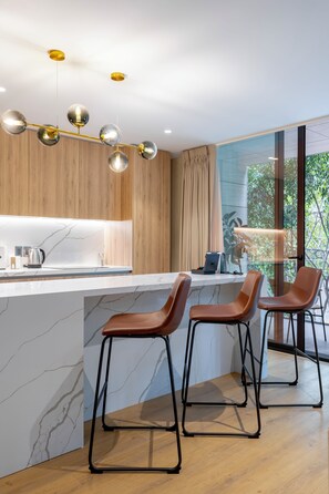 A modern kitchen with a marble countertop, wooden cabinets, and a pendant light fixture.